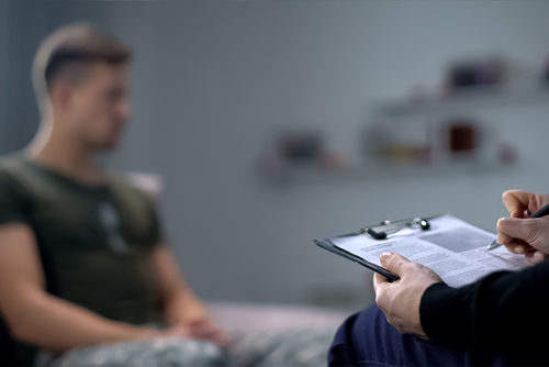 psychologist making notes during therapy session with sad male soldier, PTSD