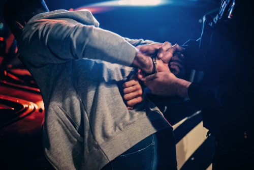 Male Policeman Forcing a Compliant Civilian on the Hood of Police Car