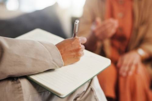 Book, counseling and hand of therapist writing notes for client with mental health evaluation