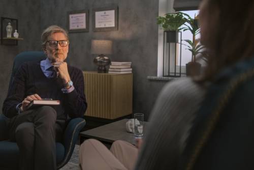 Mature psychotherapist takes notes, listens to patient, asks questions during counseling session in modern and stylish psychological office